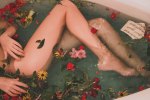 a girl with slim legs lies in a bath filled with wild flowers and ripped music sheets the water is blue the flowers are yellow pink and red with green leaves ophelia